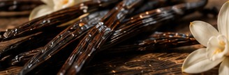 Vanilla beans and white blossoms on dark wood.